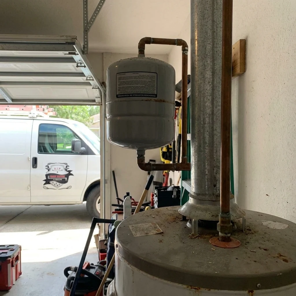 A white expansion tank mounted above a tank water heater in a garage